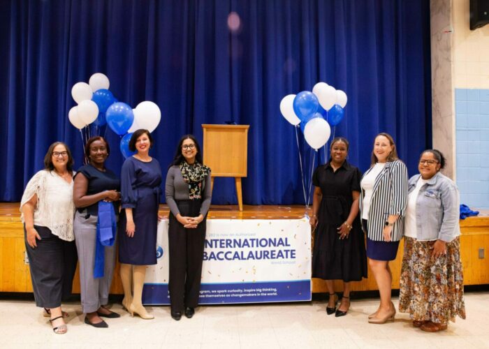 Staff and representatives pose in front of the stage at our IB blue ribbon cutting ceremony with balloons and banner in the background.