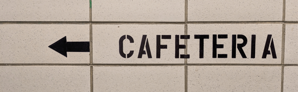 Beige tiled wall with an arrow pointing left and the word "CAFETERIA" in black letters.