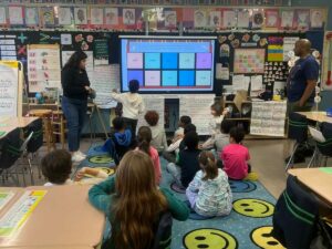 Kids sit on the floor and look at a presentation at the front of the room during a parent visit