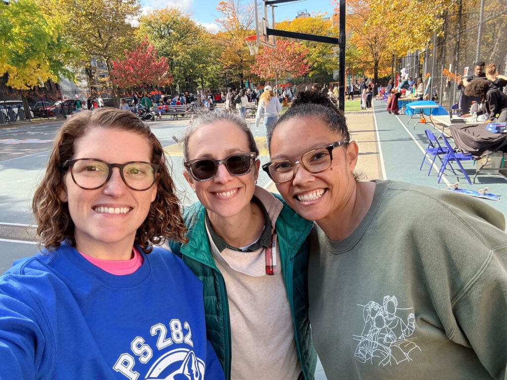 Three women smile at the camera from the playground.