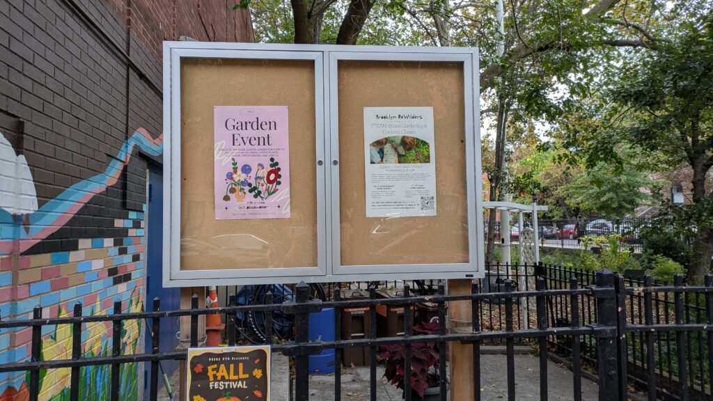 Outdoor bulletin board in front of the ps 282 garden containing two posters