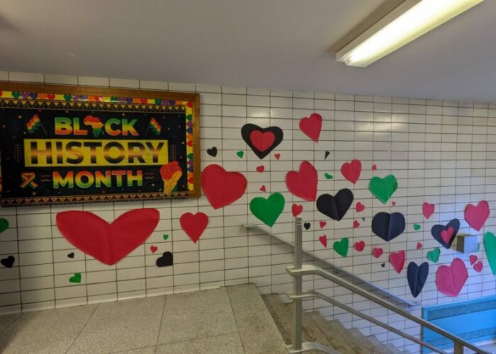 Hallway decorated for Black History Month with a colorful bulletin board and red, green, and black heart cutouts on a tiled wall.