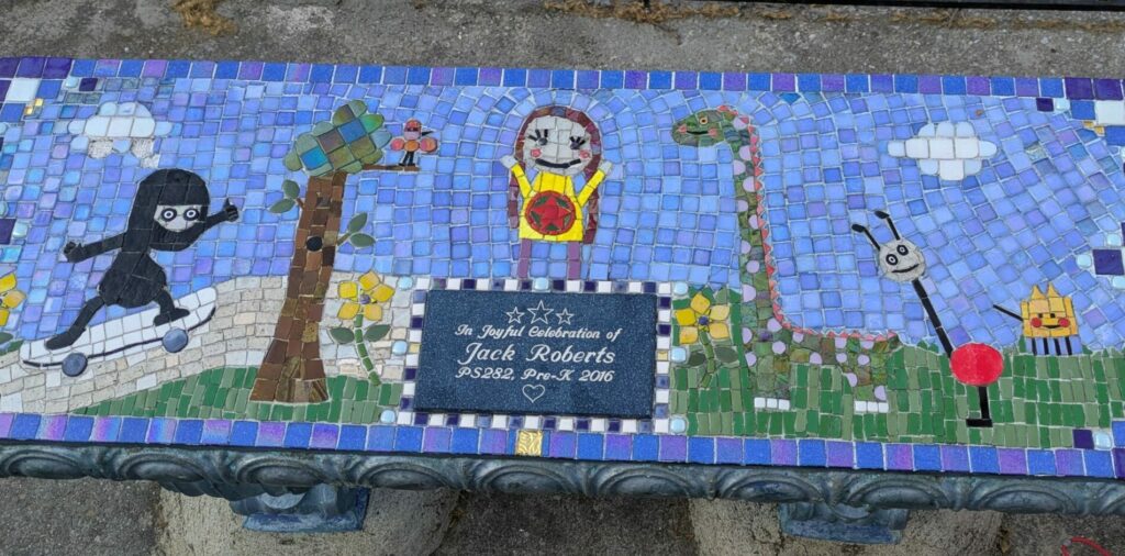 A mosaic-tiled bench with colorful designs of animals, plants, and a central dedication plaque.
