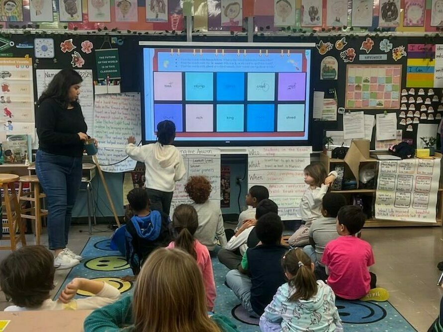 Kids sit on the floor and look at the front of the room during a parent visit