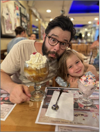 Dad sits next to daughter at a restaurant with dessert on the table