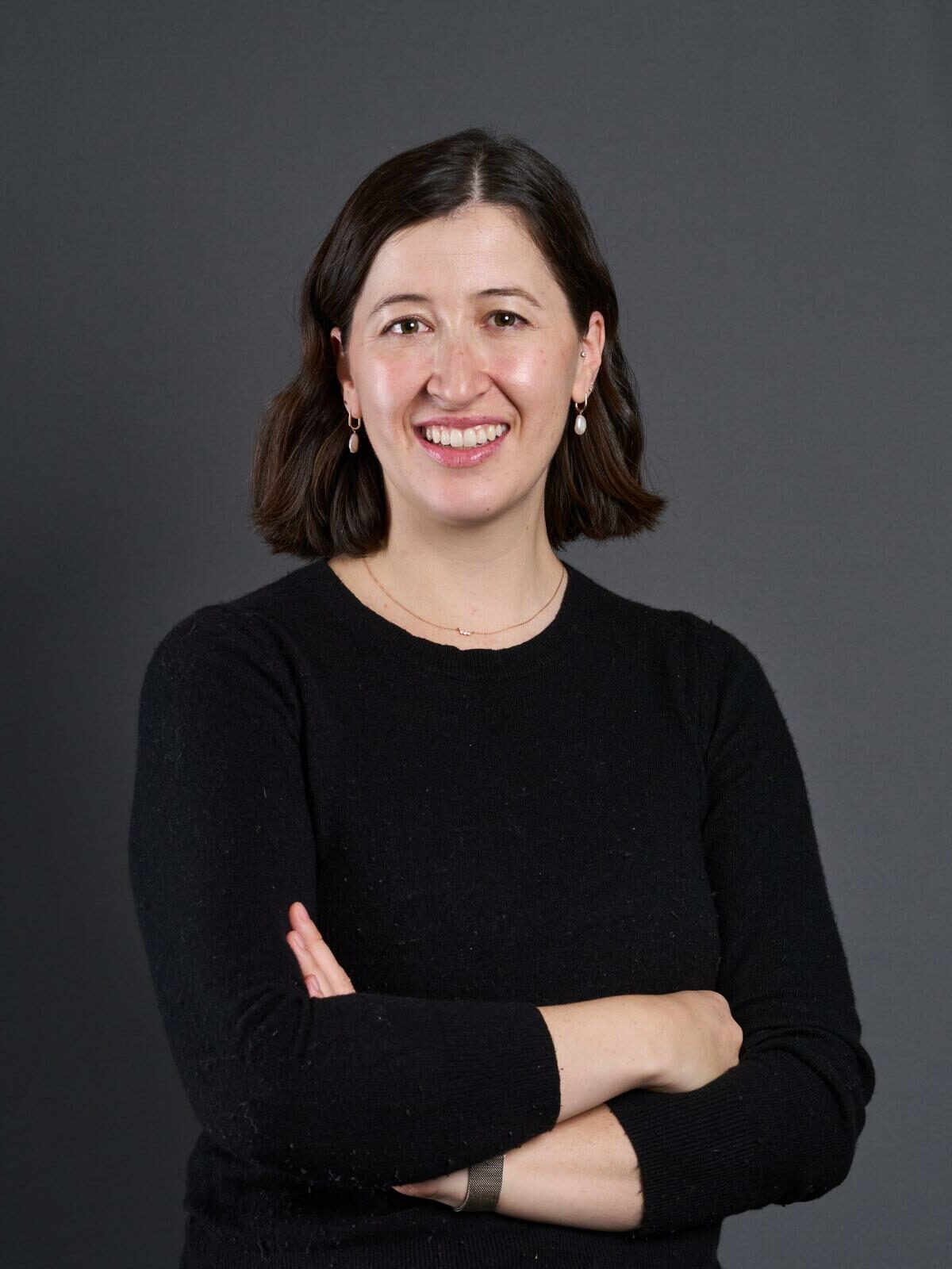 Image of woman with brown hair wearing a black shirt, crossing her arms and smiling.